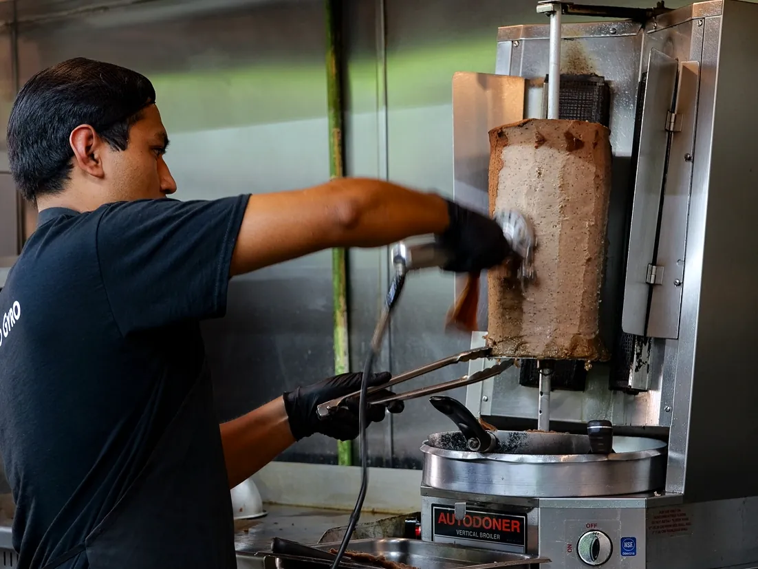 A Green Olive cook shaving gyro meat off the vertical cone